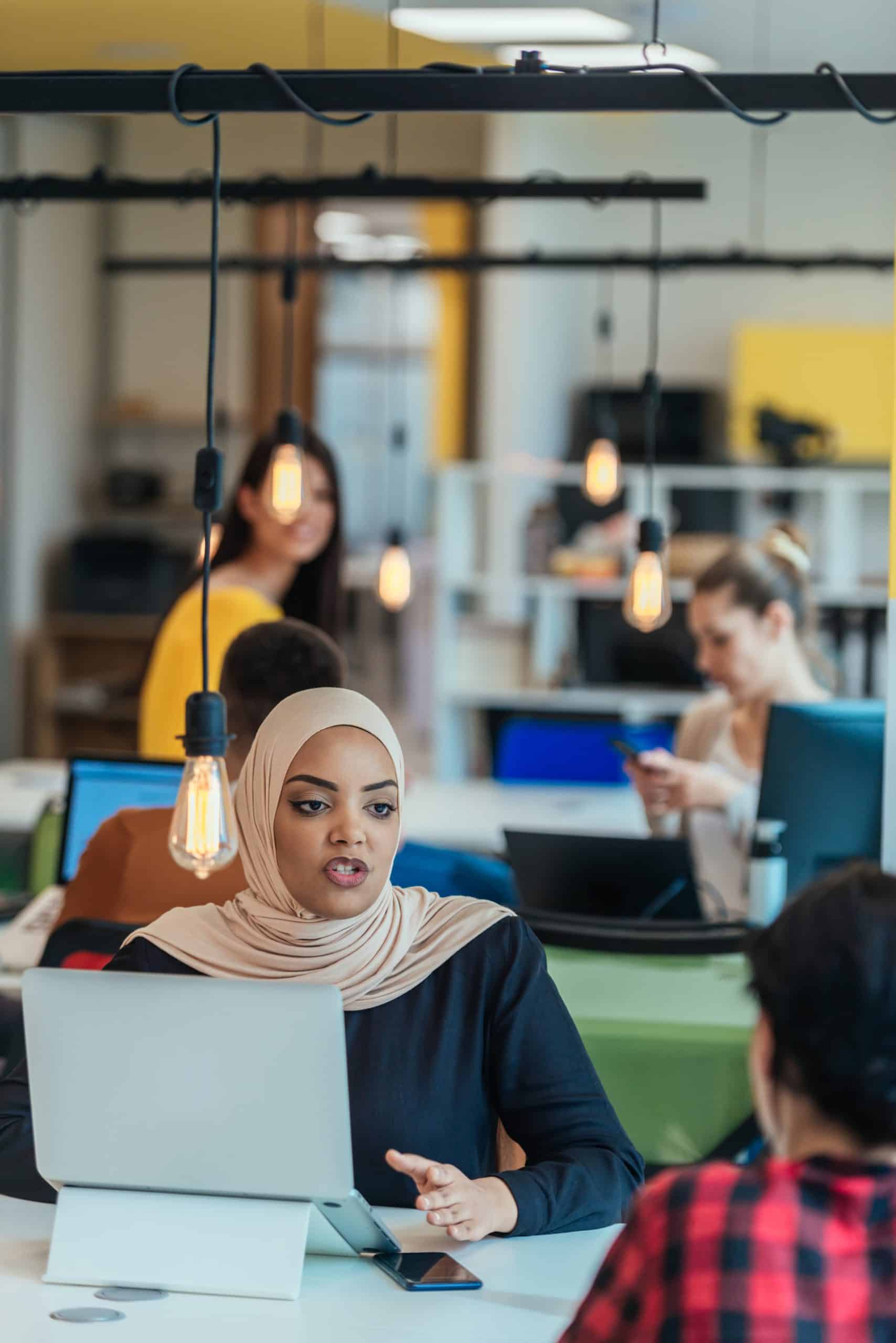 Muslim woman wearing hijab working on a laptop in a modern startup company.